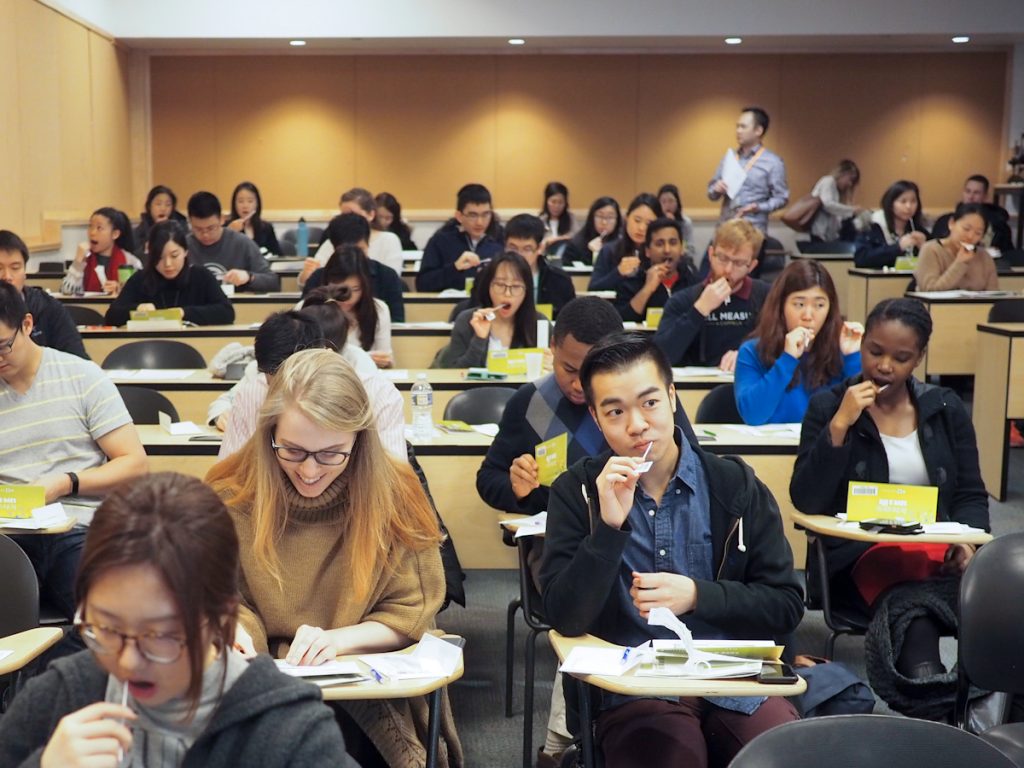 A crowd of people seated at desks swabbing their cheeks